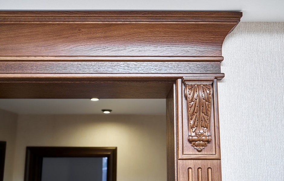 Image of a decorated wooden doorway featuring carved furniture brackets and crown molding in a craftsman style.