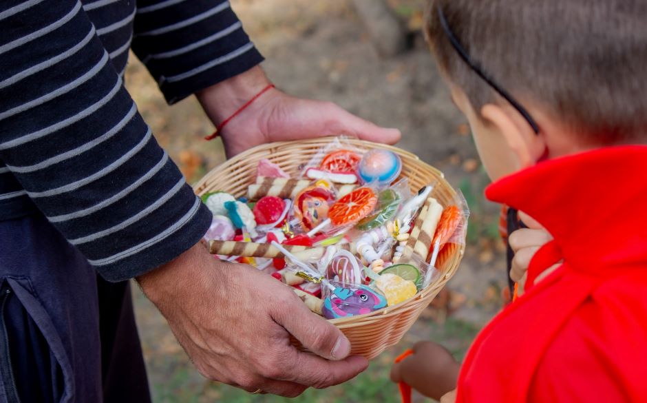 Lady holding a basket of typical Halloween candies and giving them to a child