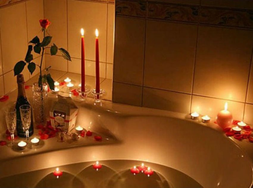 A single rose and different kinds of candles with glass holders and loose petals create a romantic atmosphere. Image Source: Writeens