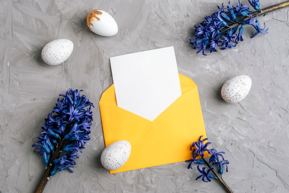 Yellow envelope with blank paper, some decorated eggs, and three branches of blue flowers