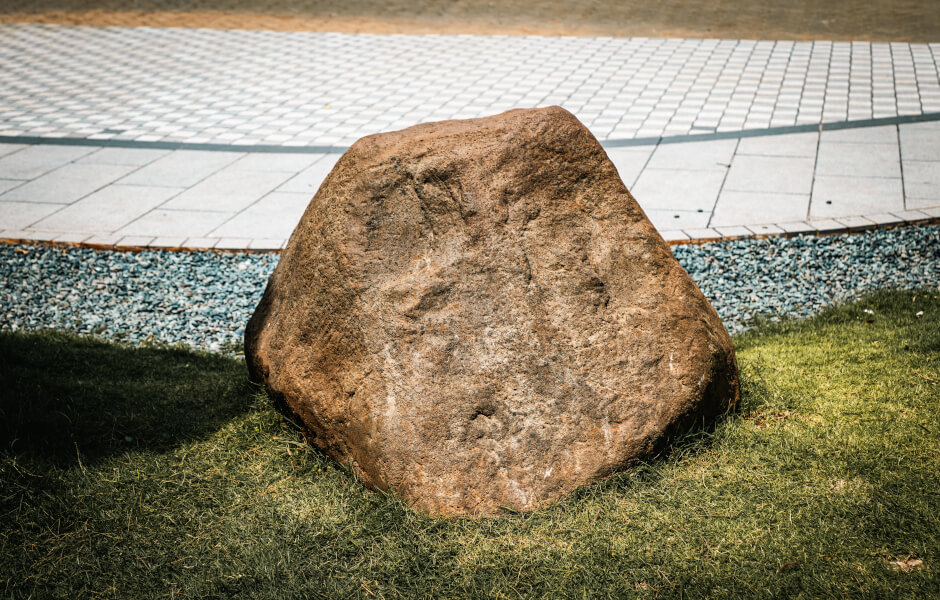 Image of a large stone set in a garden, resting on a grassy area.