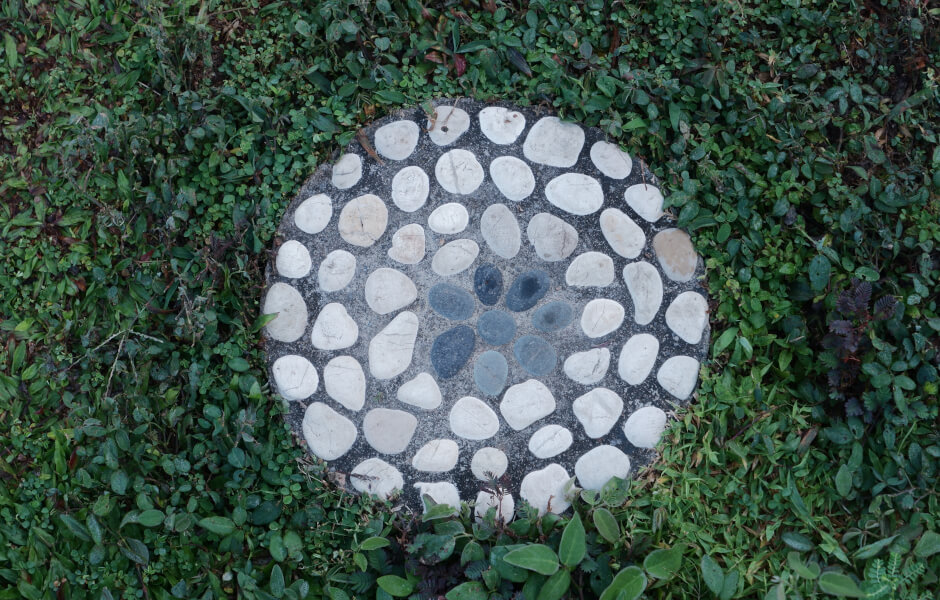 Image of a circular stone mosaic stepping stone set in a bed of green grass.