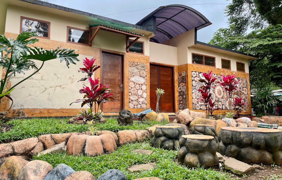 Image of a yard with plants and rocks, including flat stones and a bench for seating, surrounded by plants and smaller rocks.