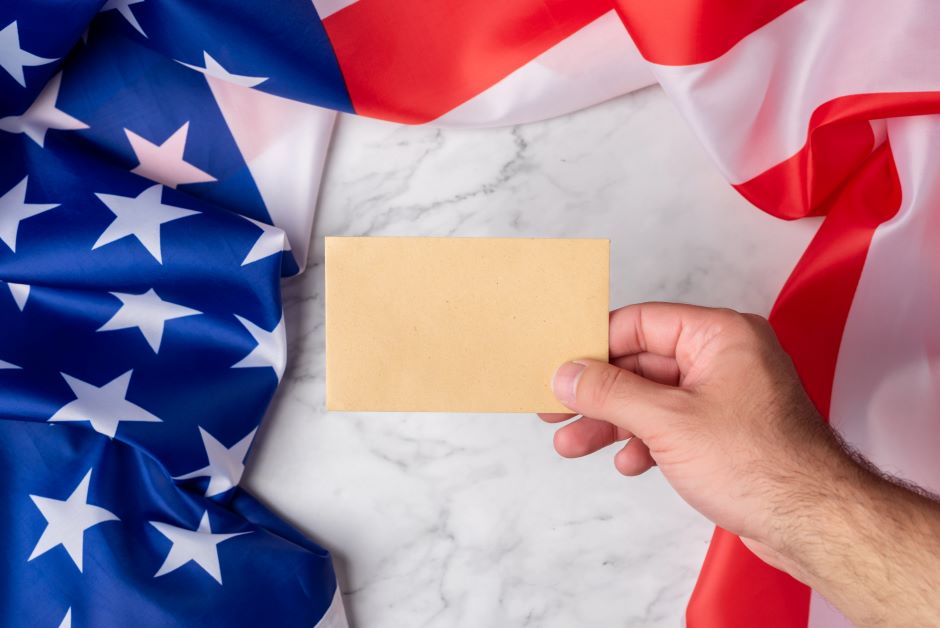 Hand holding a blank card with an extended american flag on the table