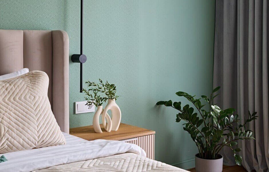 Modern bedroom with green walls, bed with upholstered headboard, wooden bedside table, and decorative plants.
